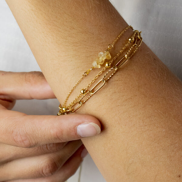 Bracelet en chaines mailles trombones et forçats en acier inoxydable avec fermoir bouée et perles de citrine, porté sur un poignet en gros plan