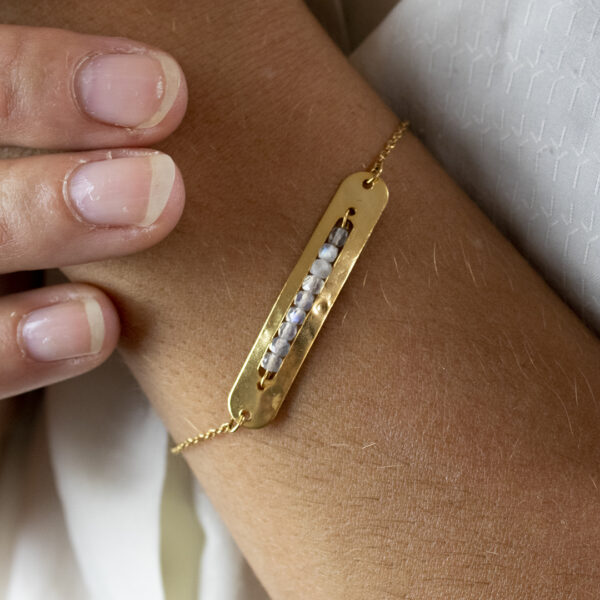 Bracelet avec un connecteur de forme rectangulaire arrondie, contenant des perles de labradorite, porté sur un poignet en gros plan