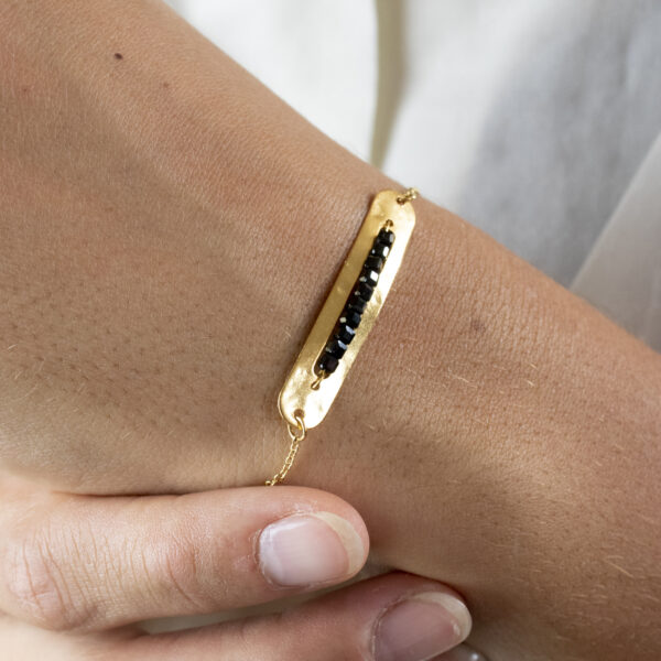 Bracelet avec un connecteur de forme rectangulaire arrondie, contenant des perles de spinelle, porté sur un poignet