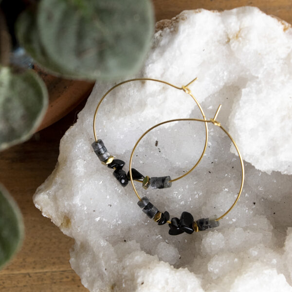 Boucles d'oreilles créoles en perles d'agate noire et larvikite posée sur une géode