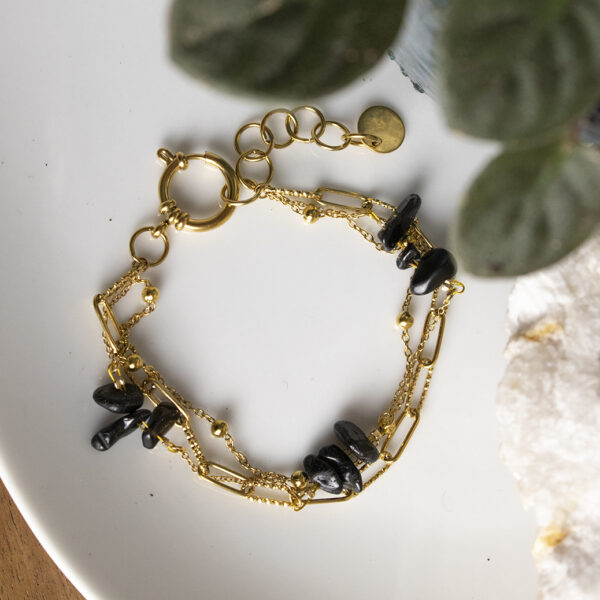 Bracelet en chaines mailles trombones et forçats en acier inoxydable avec fermoir bouée et perles d'agate noire, posé sur une assiette avec des feuilles qui dépassent sur le côté