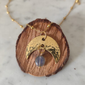 Pendentif en forme de lune en laiton martelé et perle de labradorite avec une chaine maille forçat et boules sur un rondin de bois