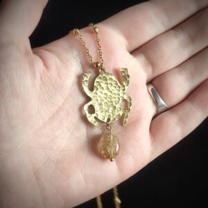 Main portant un pendentif en forme de scarabée en laiton martelé et perle en citrine