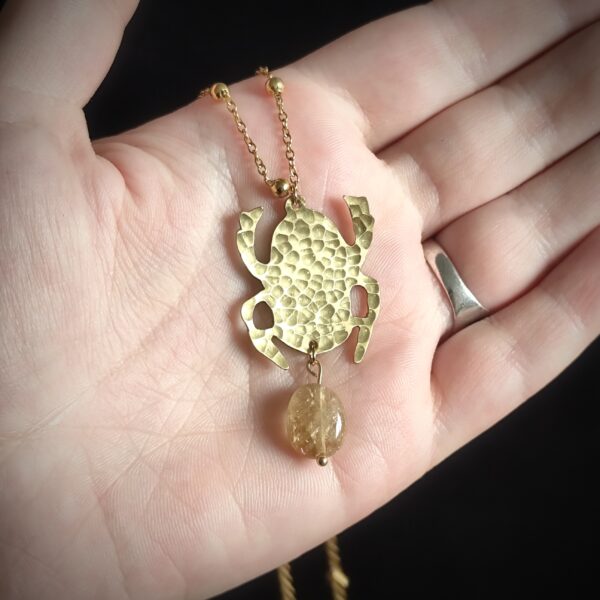 Main portant un pendentif en forme de scarabée en laiton martelé et perle en citrine